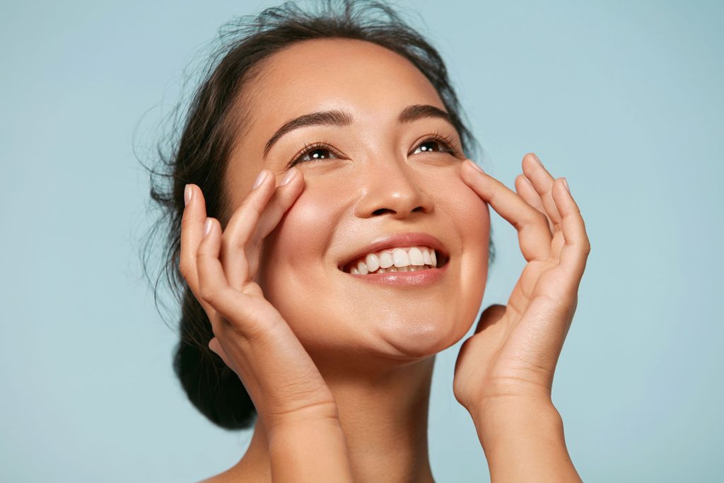 Smiling woman gently pressing the skin under her eyes, symbolising rejuvenated complexion after REJURAN® polynucleotide treatment.